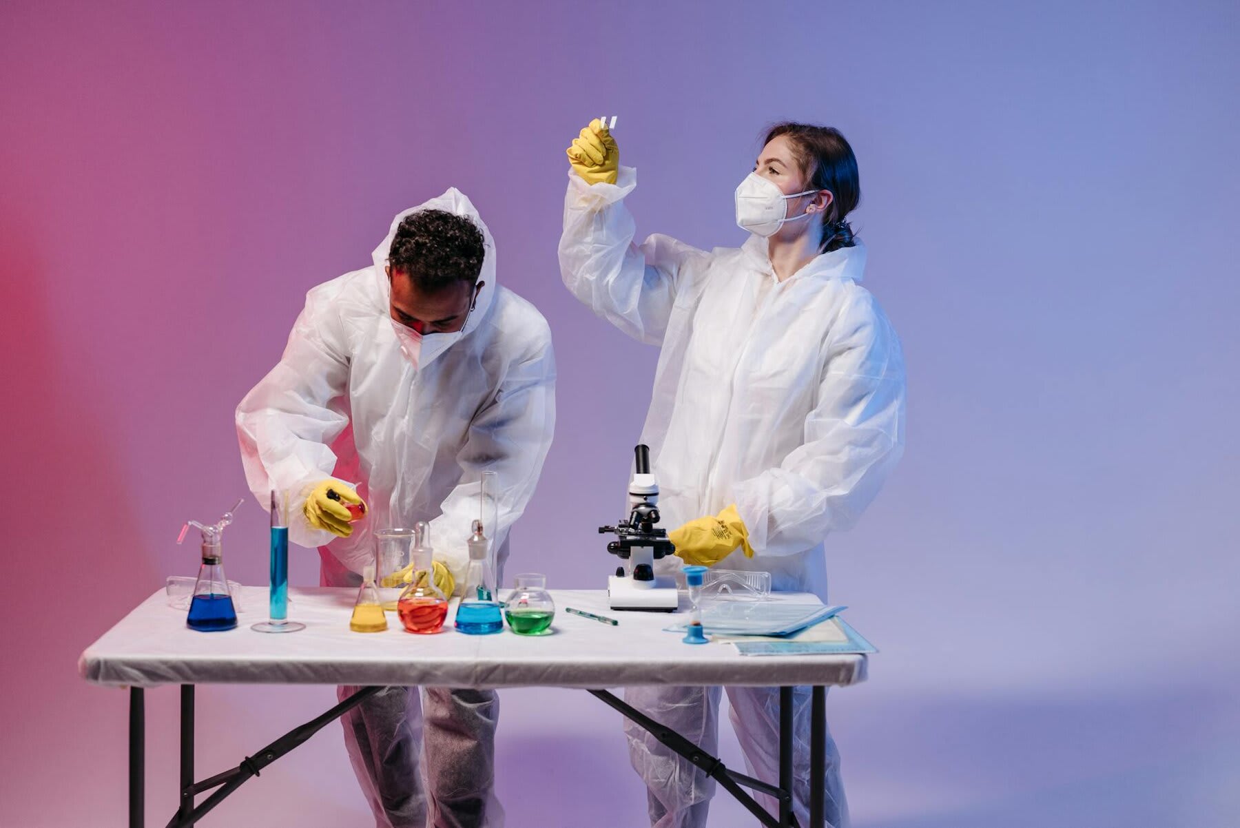 Two individuals in lab coats and masks collaborating on a table, engaged in scientific work