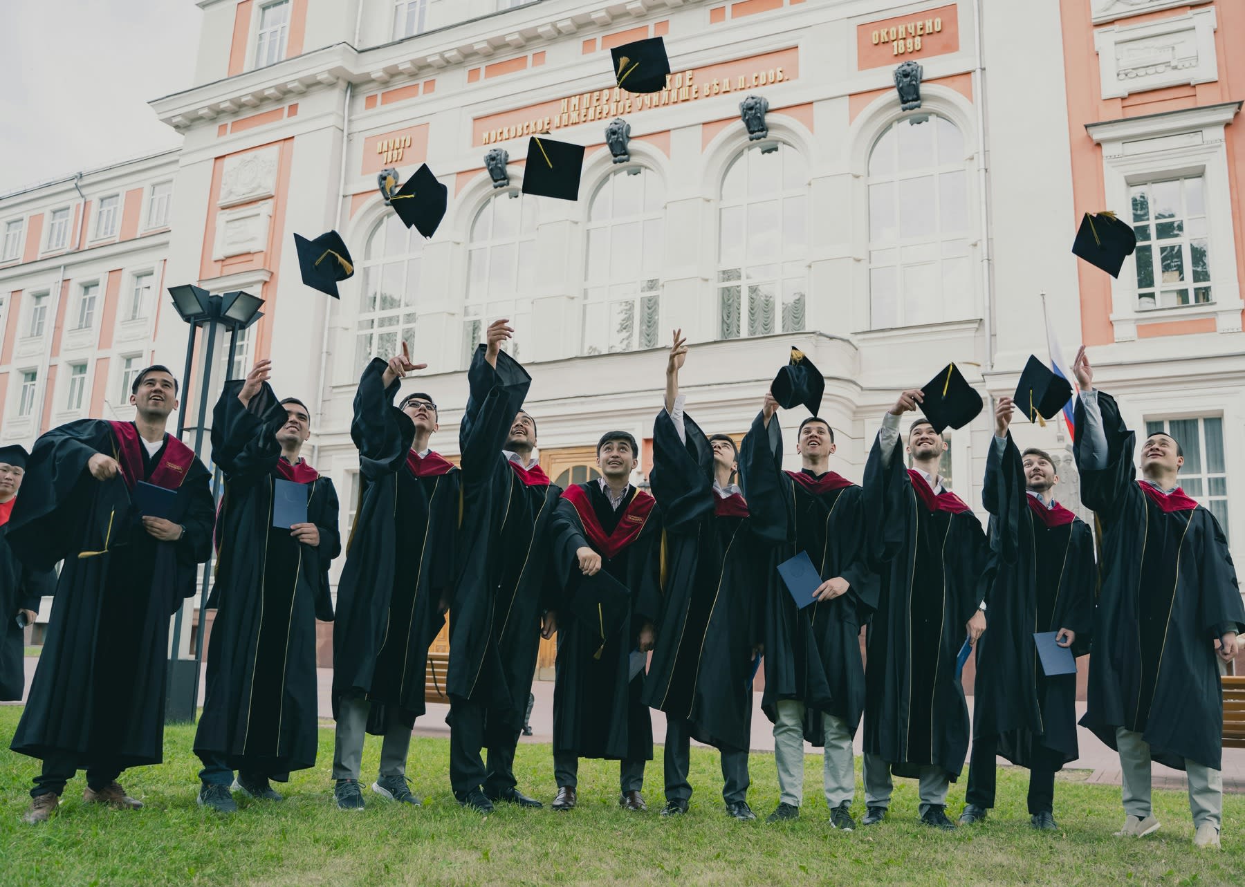 Group of graduate students wearing graduation robes, all throwing their caps in the air