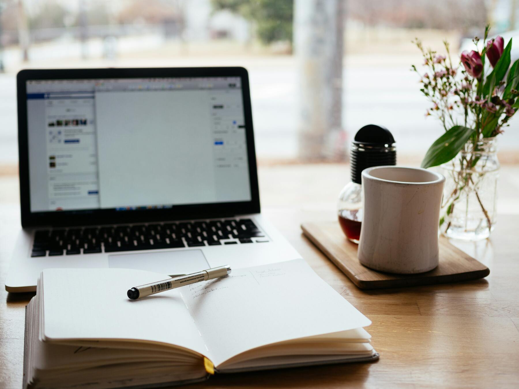 Laptop with an opened notebook, coffee mug and pencil