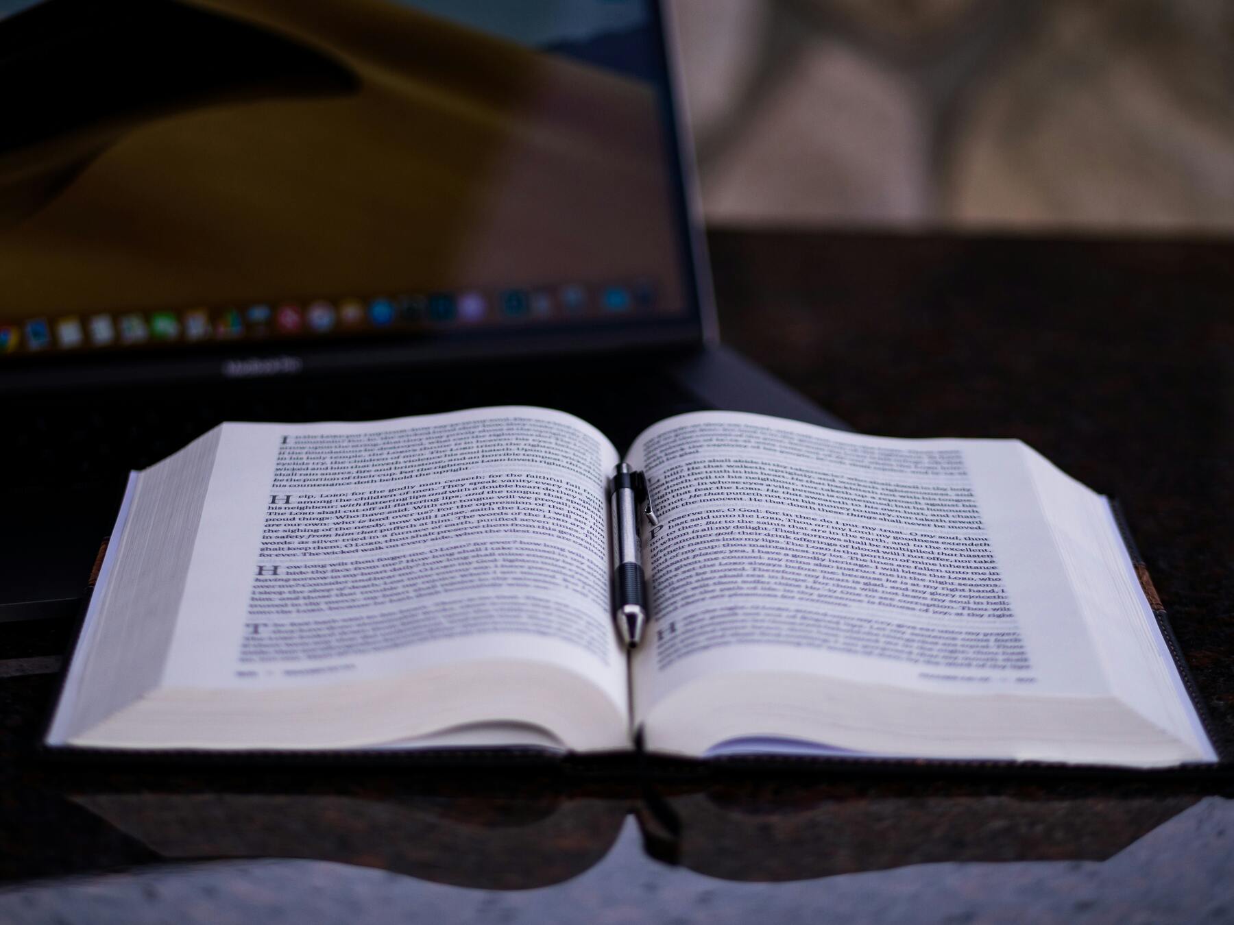 Opened book and pen with a laptop on the table