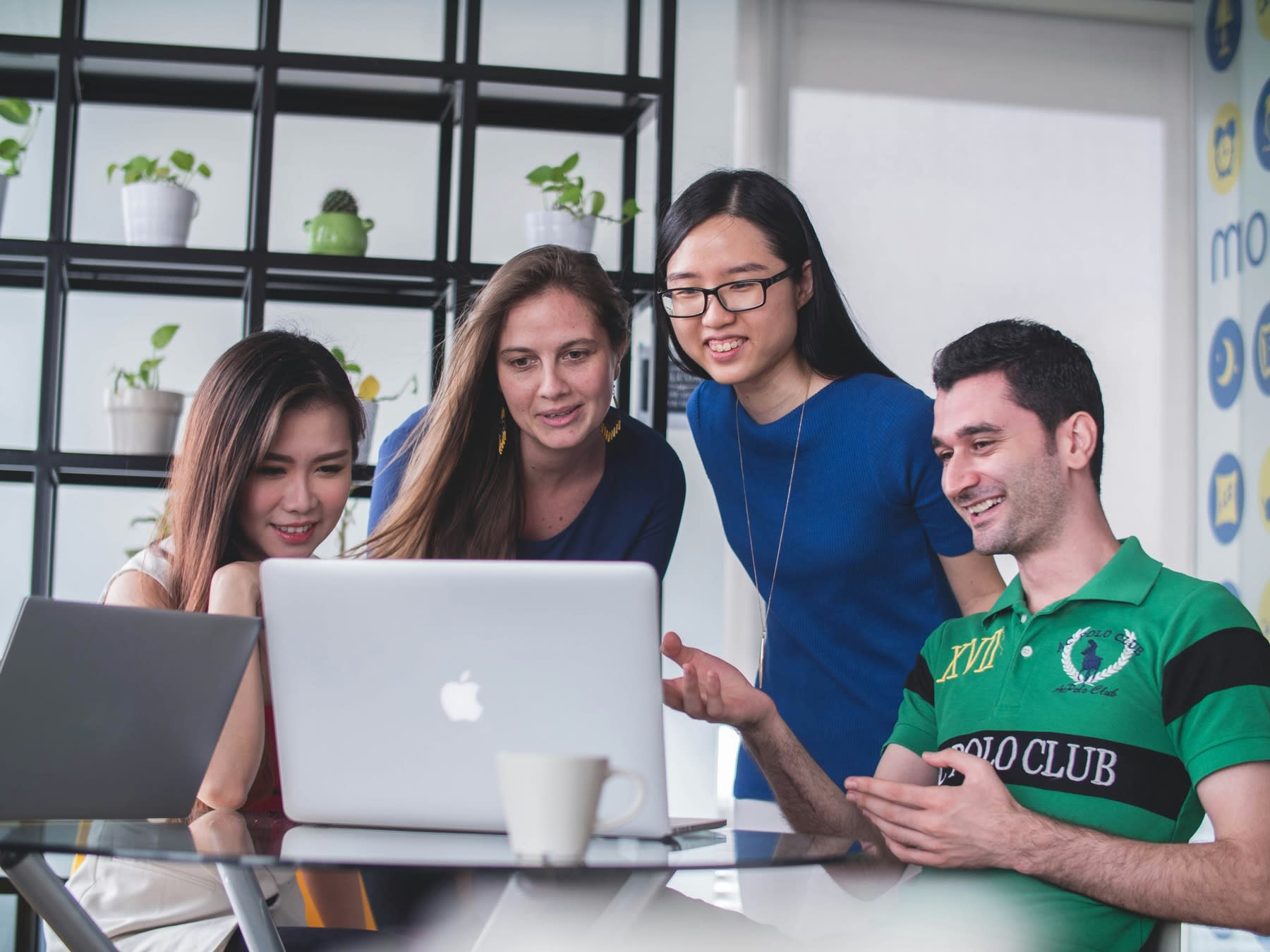 Students gathered around a table looking at the same laptop screen