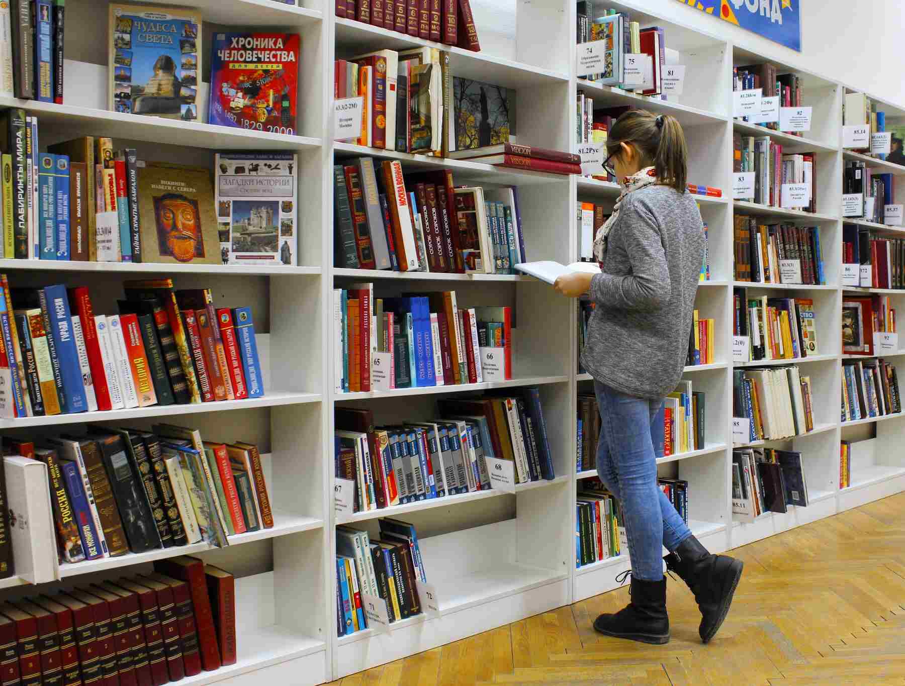 Woman reading a book in front of a library shelf
