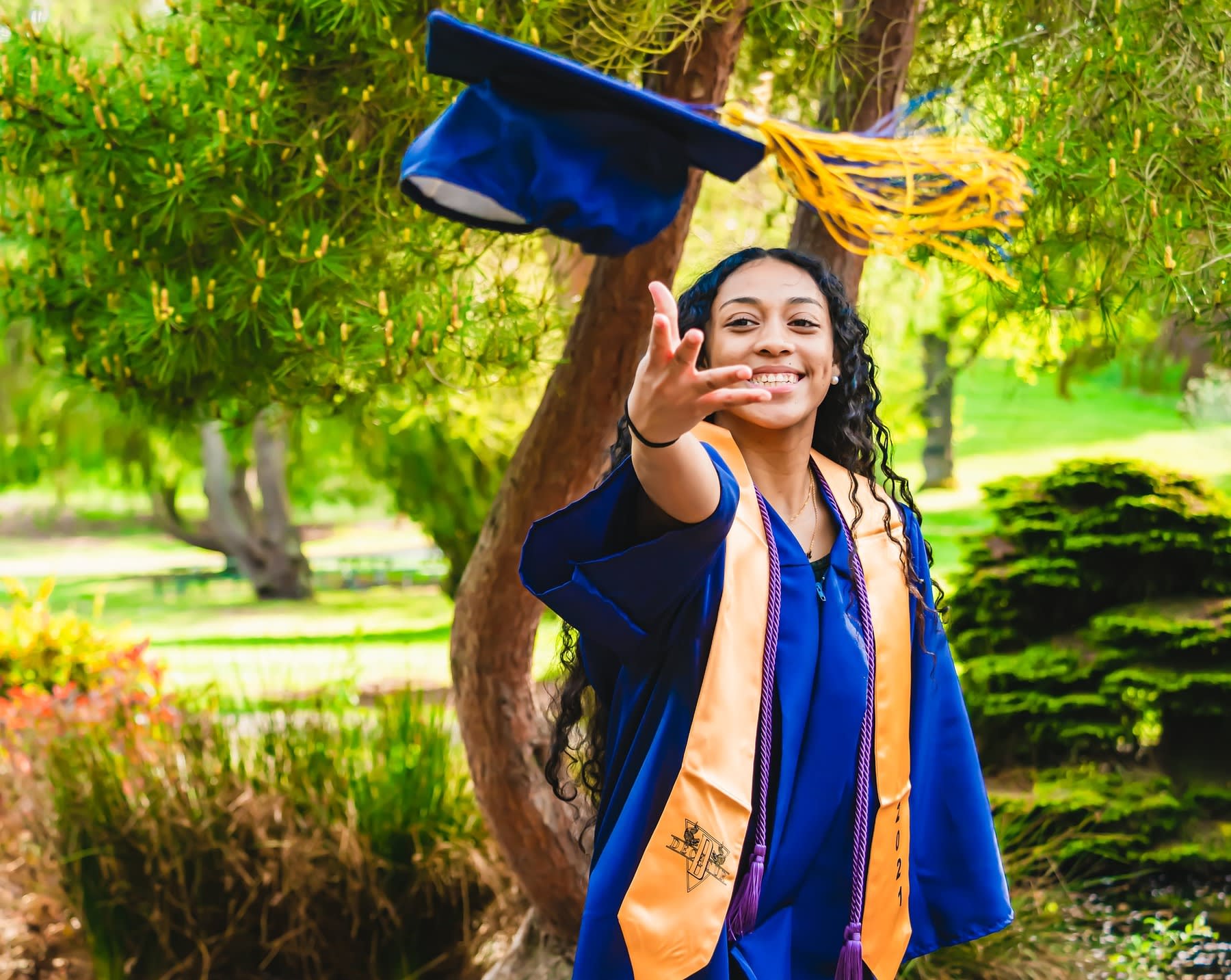 Woman wearing graduation robes while throwing her graduation cap in the air