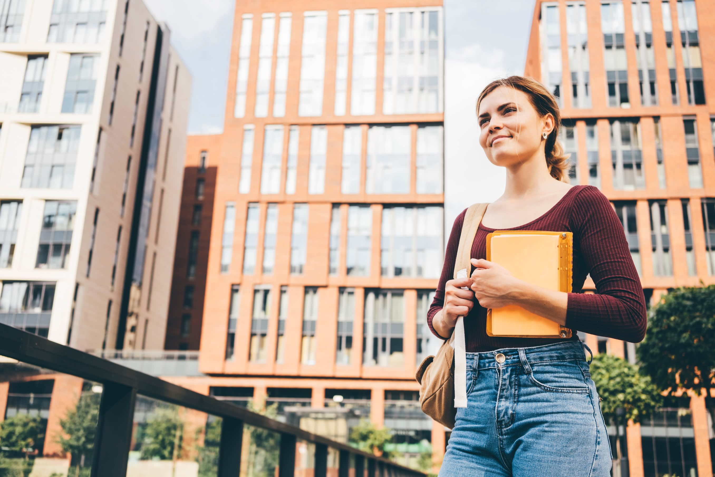 Happy female student with a notebook walking in a city