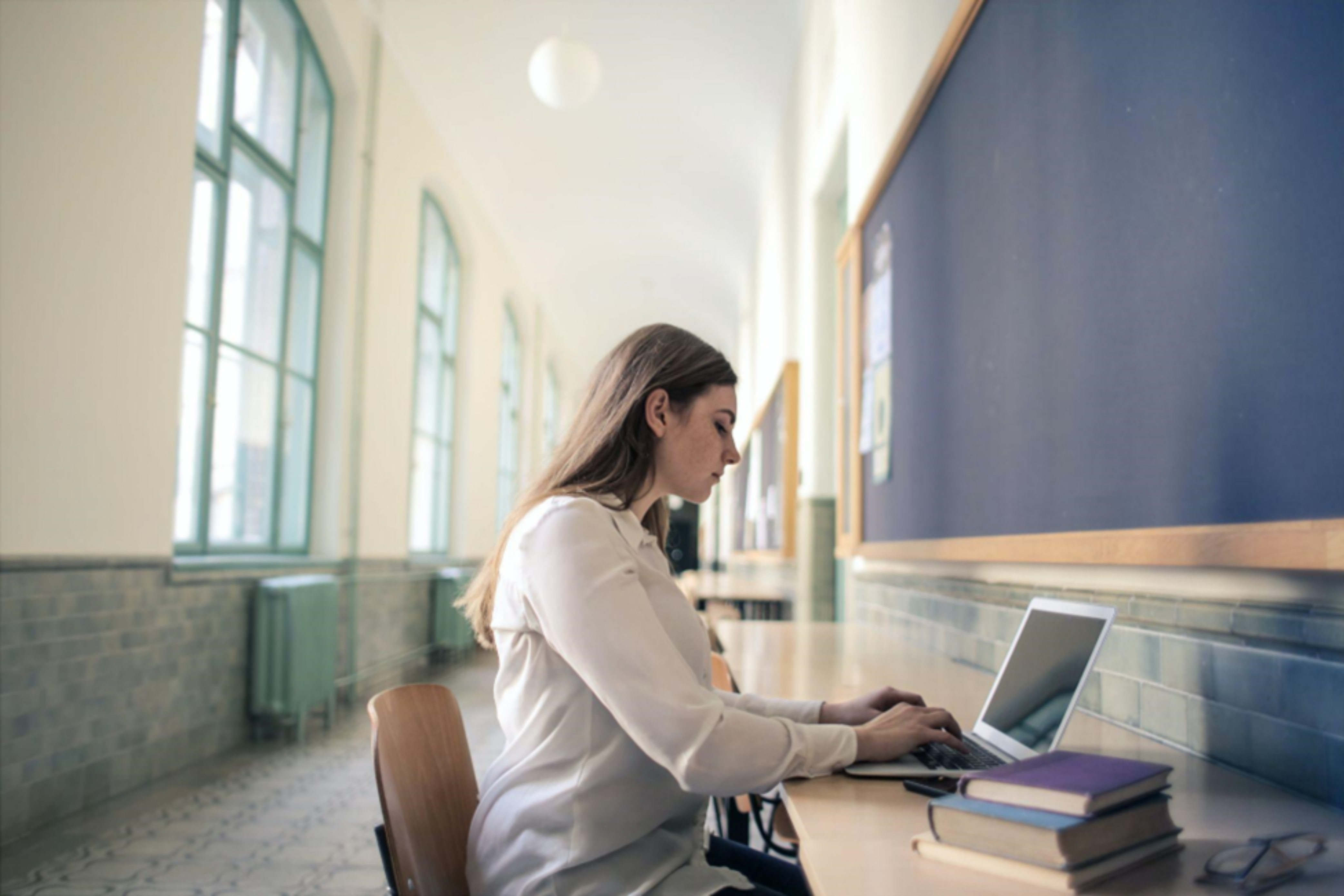 Professor of special education psychology seated in a school corridor typing on a computer