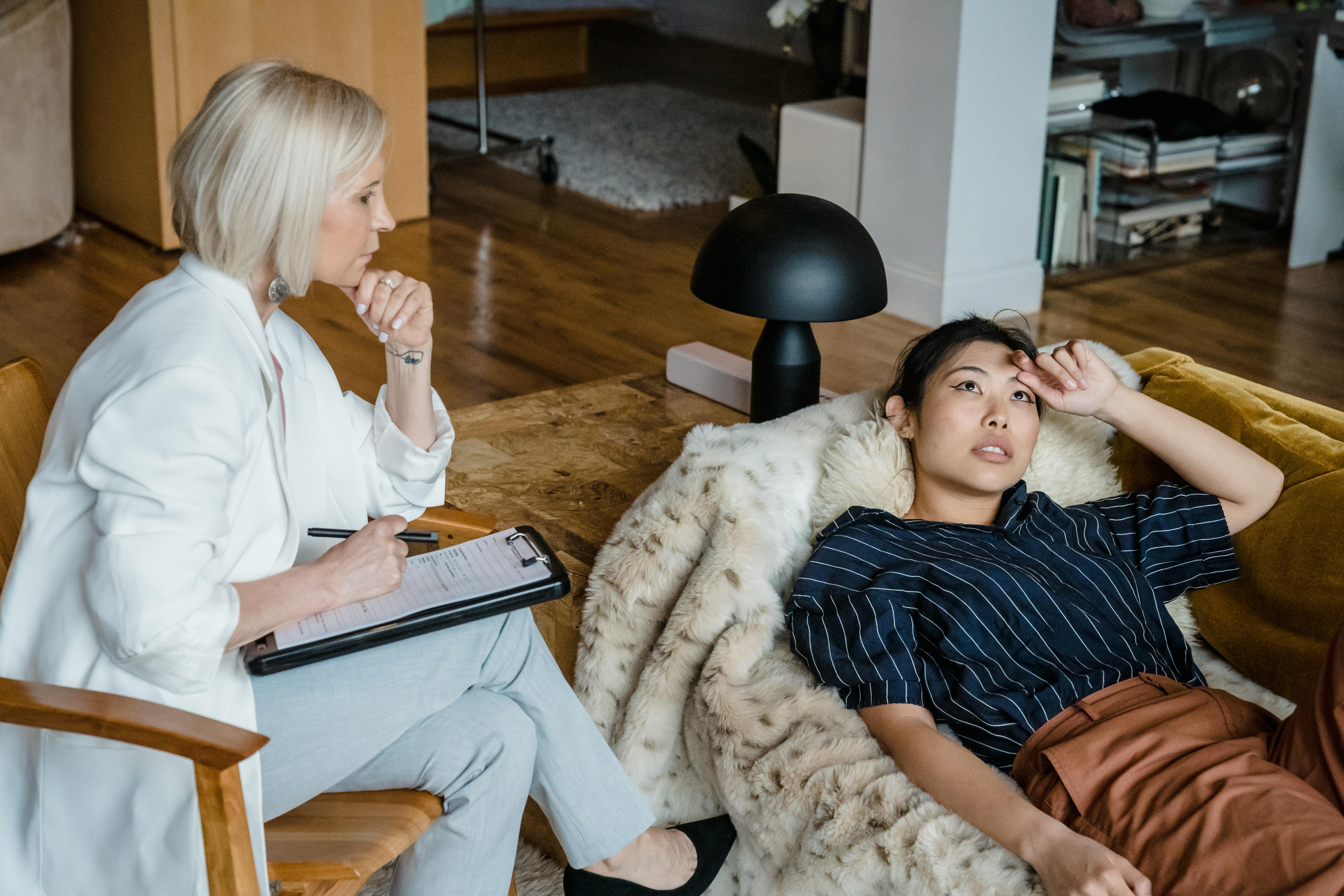 Woman lying on a sofa couch while her therapist listens to her during their session