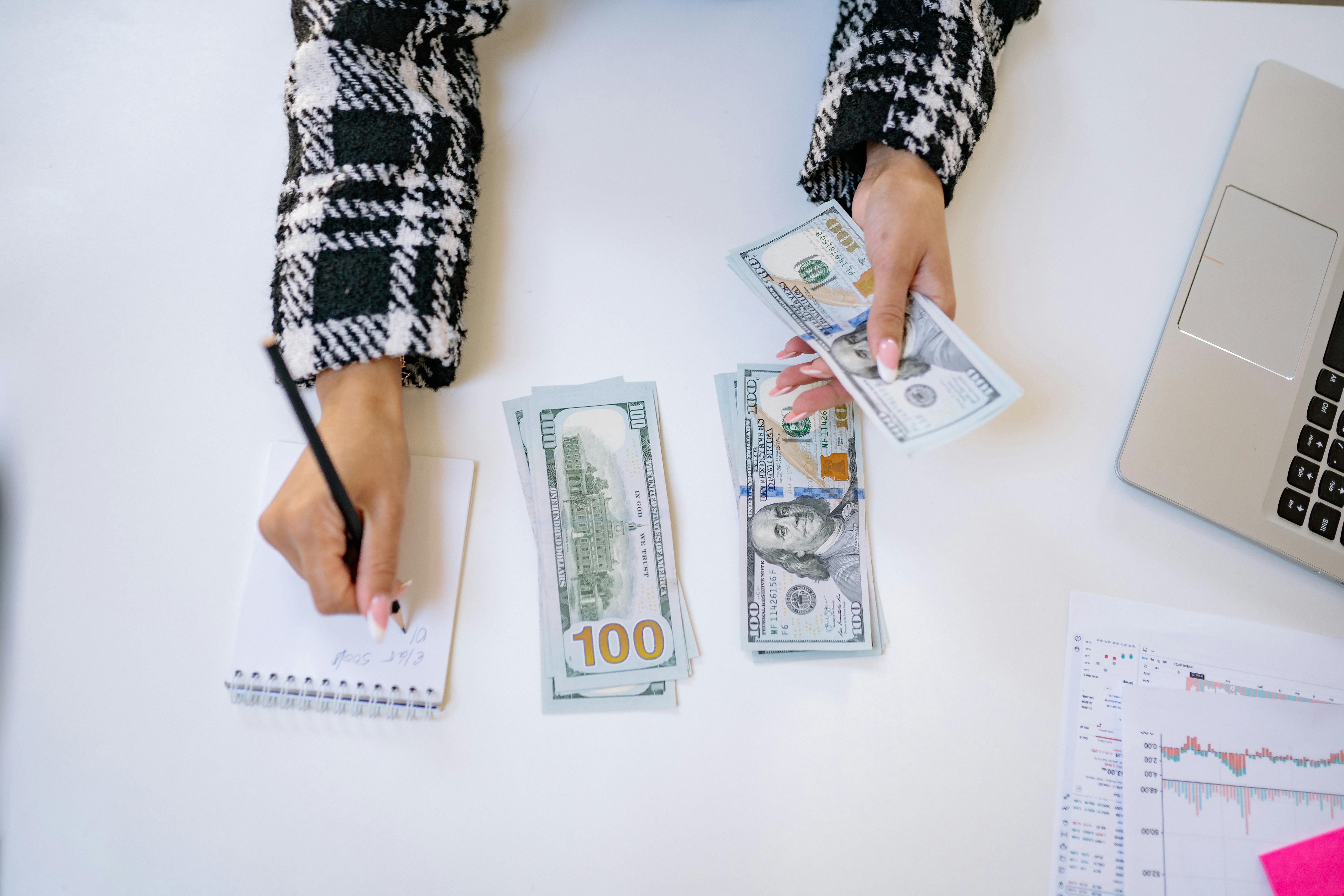 Woman counting dollar bills while writing on a notepad