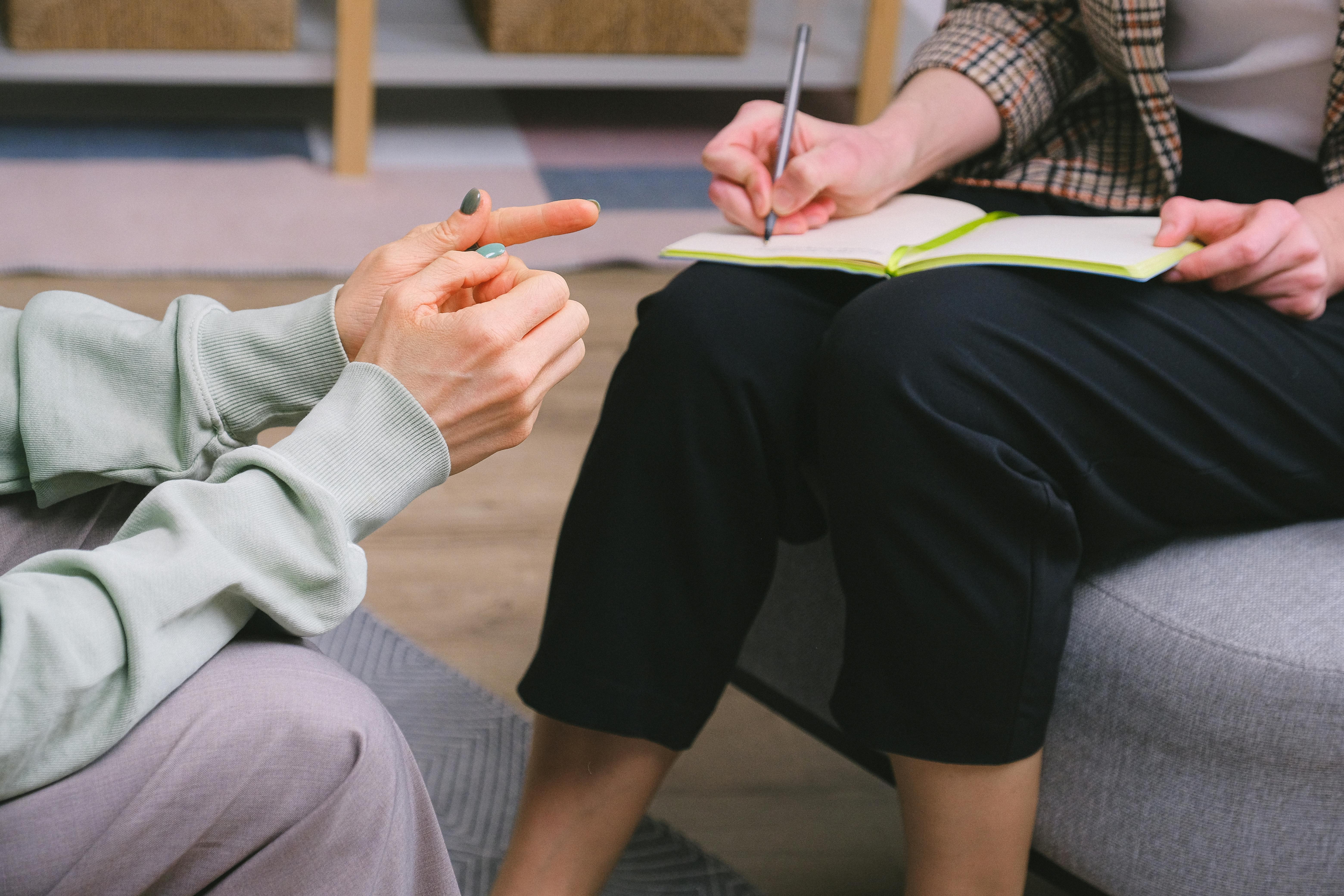 Woman writing down notes on her notebook, while sitting on the opposite sofa from her boss