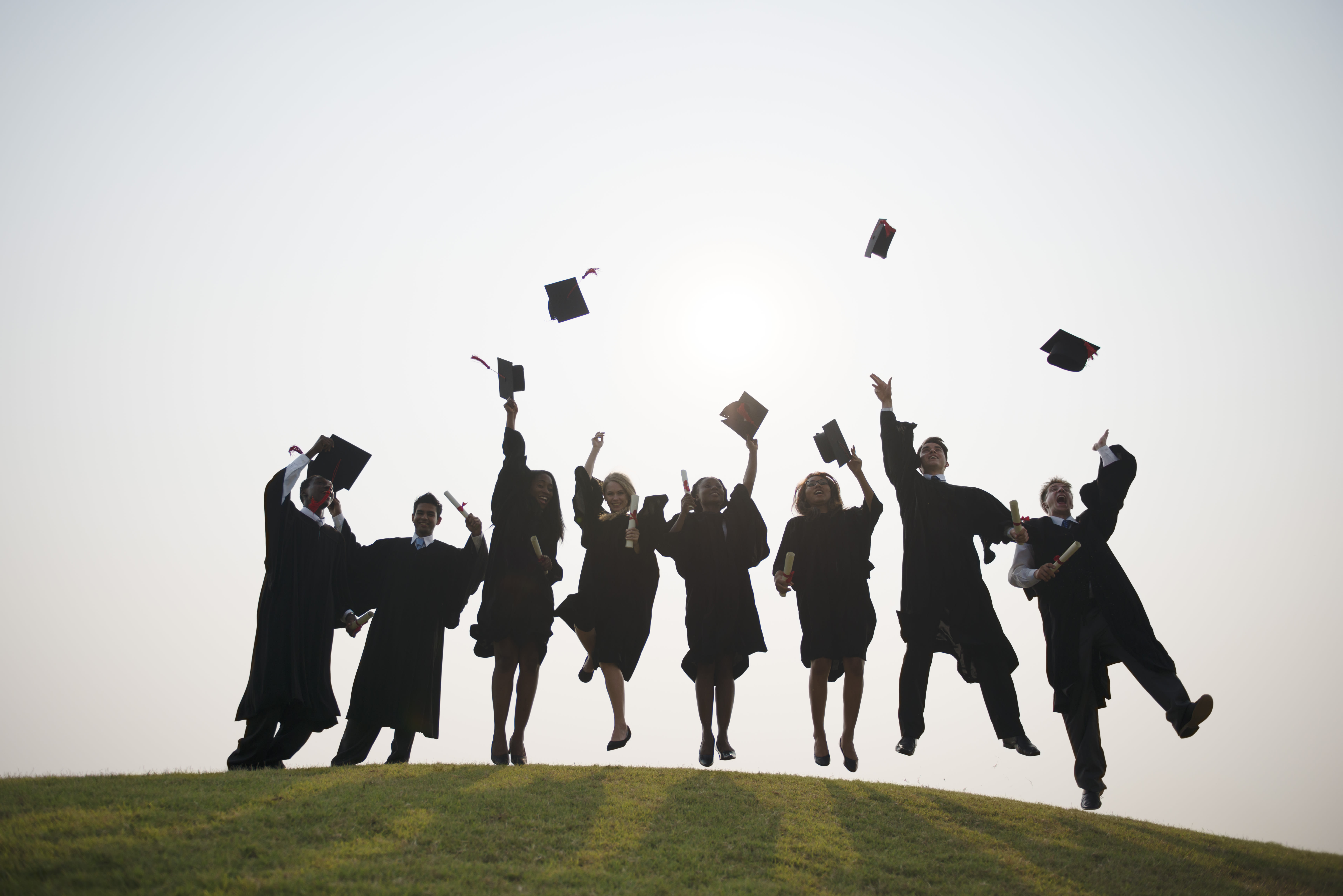 Graduates jumping in a field with cap and gown