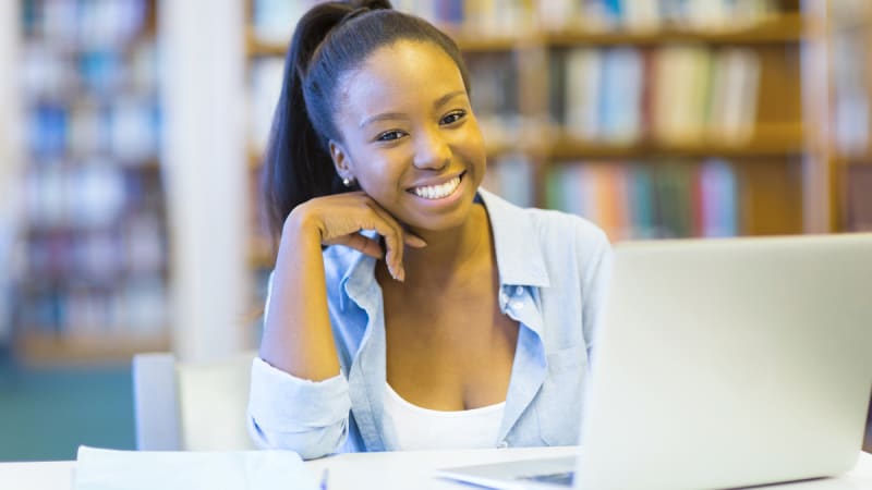 Woman smiling at laptop in library