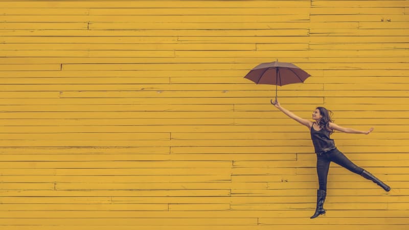 Woman jumping with an umbrella in front of a yellow building