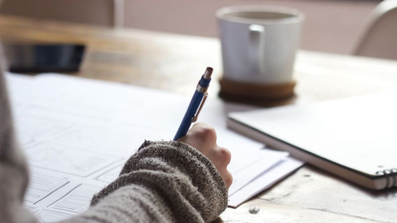 Person writing next to a cup of coffee